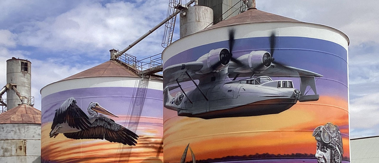 Mural of Catalina flying boat and pilot painted on 2 grain silos with sky in the background