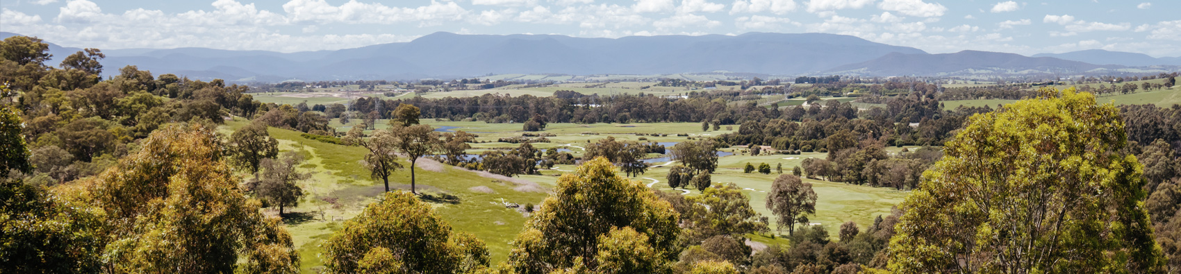 A panoramic landscape of rural Victoria with grass, hills and clouds.