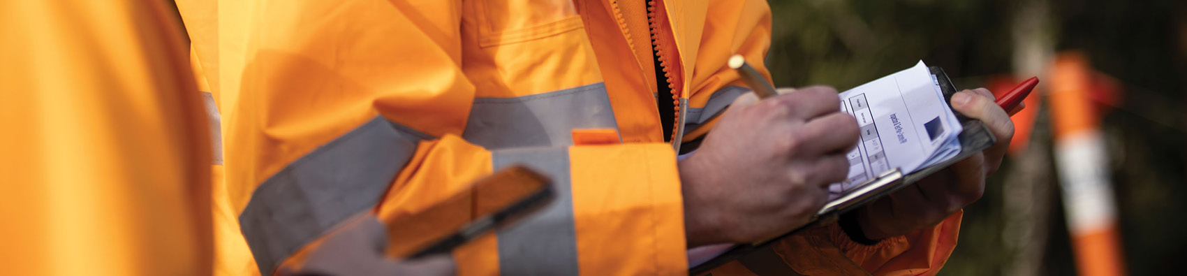 Two people wearing hi vis safety jackets. One person is holding a document and writing on it with a pen.