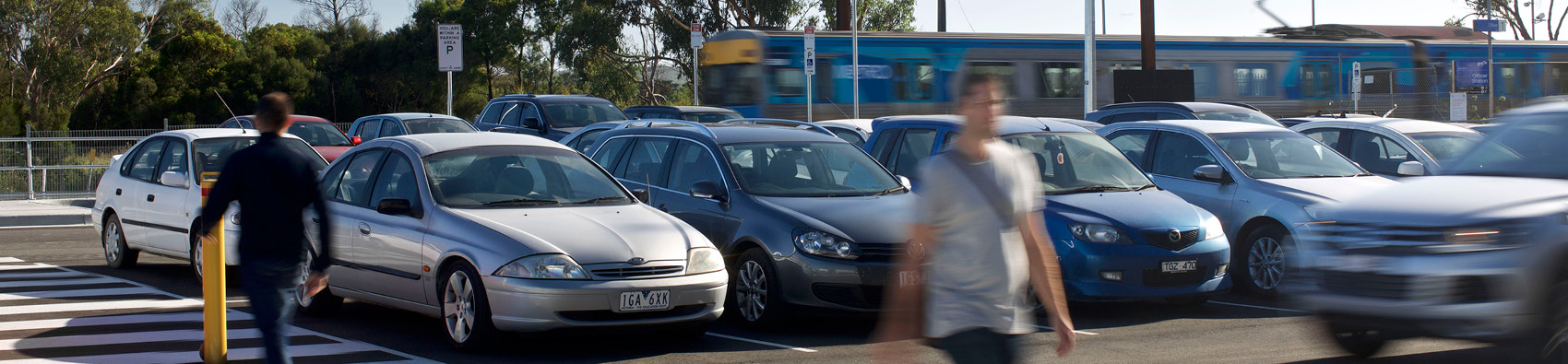 Two people walking on a pedestrian crossing in a train station car park.