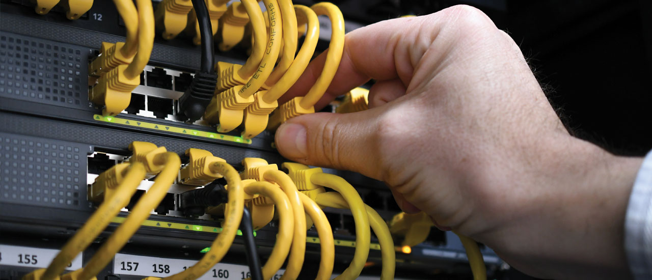 A hand touching ethernet cables sitting in some telecommunications equipment.