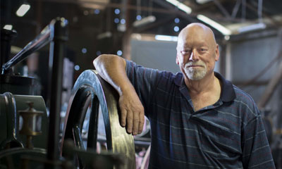 A person leans on the wheel of heritage railway equipment in a goods shed while looking towards the camera.